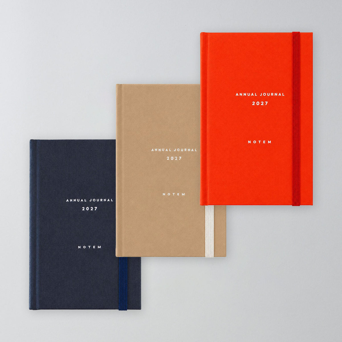 Drei A6 Jahreskalender 2027 nebeneinander in Navy, Rot-Orange und Sand
