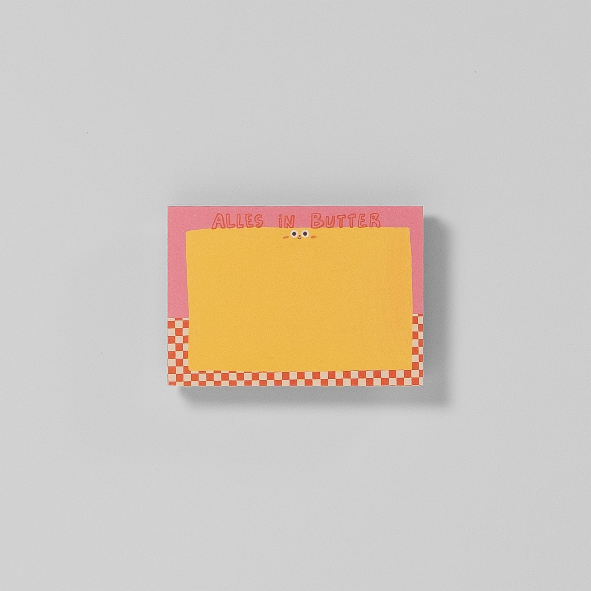 Notizblock A7 „Alles in Butter“ von Illustratorin Slinga – pinker Hintergrund, gelber Butterblock mit Kulleraugen, roter Karo-Rand