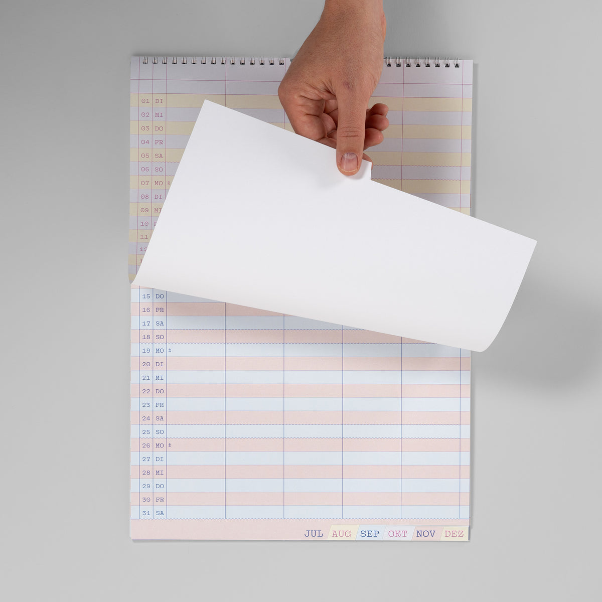 Hand blättert im Familienkalender 2027 von Juni zu Juli, Wire-O-Bindung