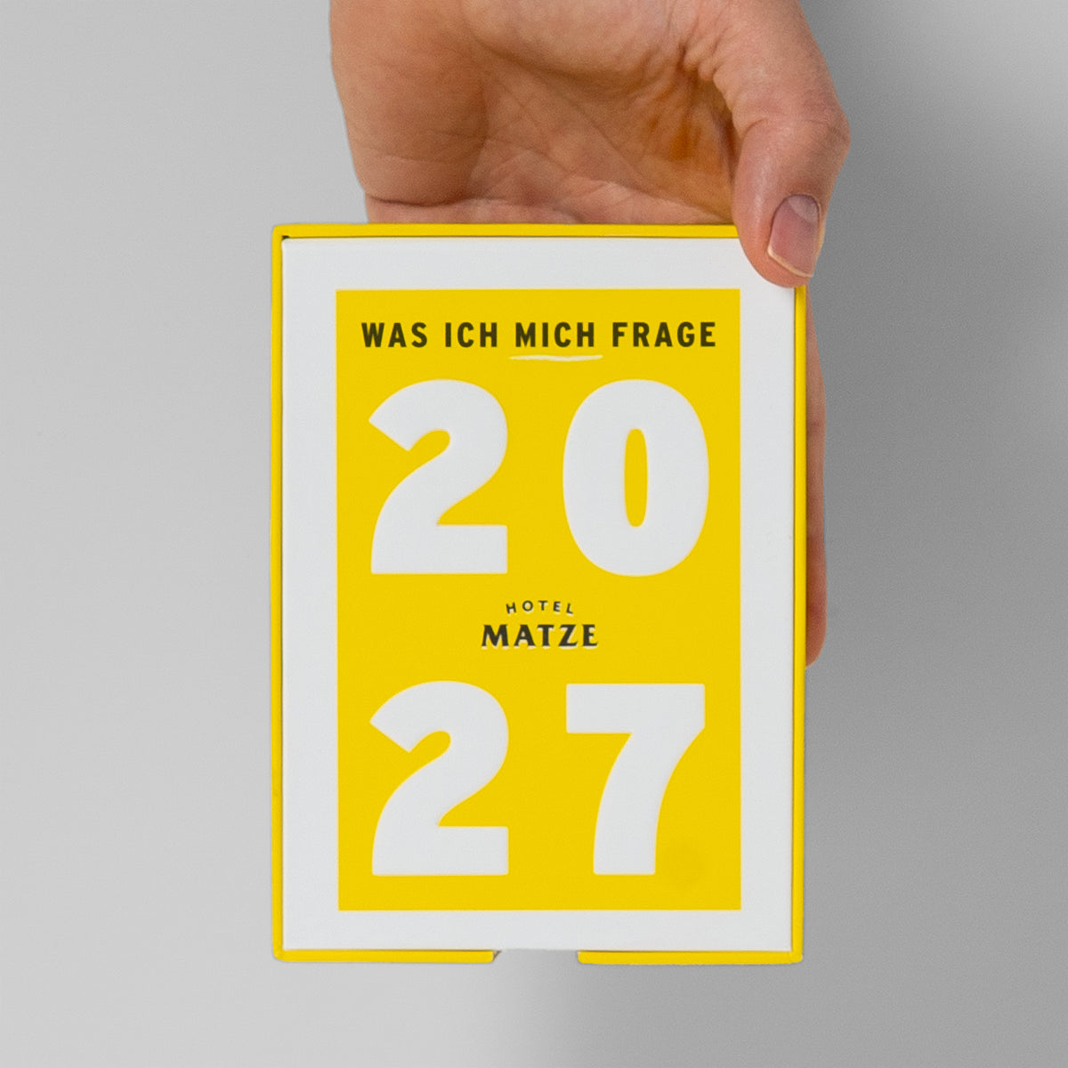 Eine Hand hält die gelbe Box des Fragenkalenders: handliches Format im Größenvergleich