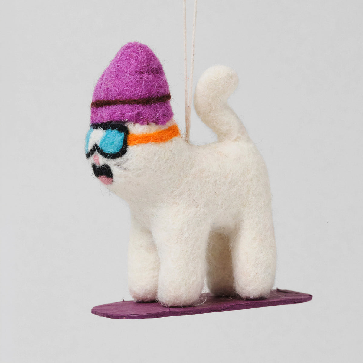Wrap Filzanhänger Snowboarder Shaun: weiße Filzkatze mit lila Mütze und Skibrille auf einem lila Snowboard